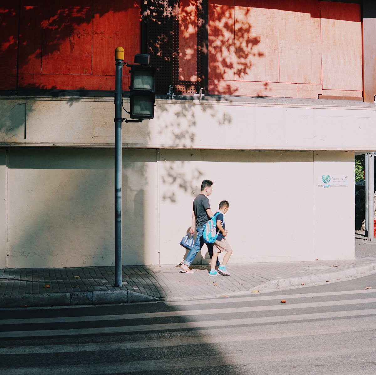 edwardesmir's tweet photo. Lunch break street snap: a kid chasing a stray cat on a tree-lined alley, passersby smiling in the warm afternoon glow. https://t.co/ouNt5ih4VD