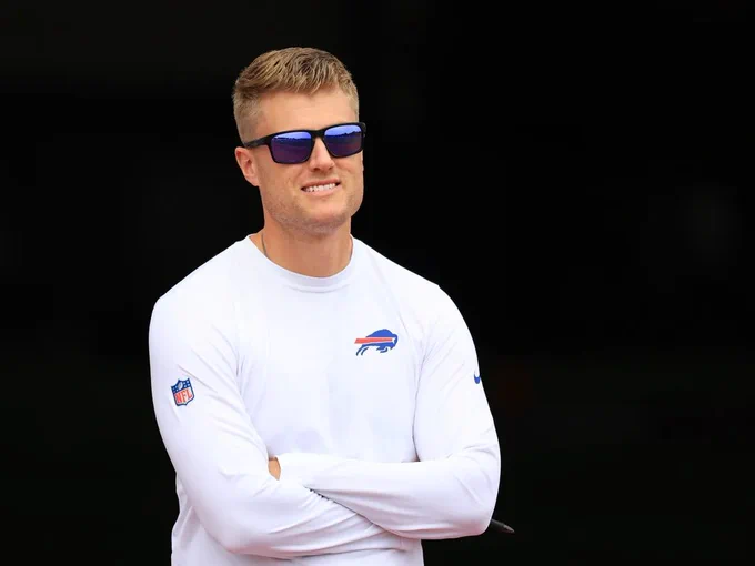 a man wearing sunglasses stands with his arms folded wearing a buffalo bills shirt