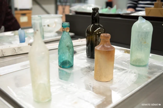 Five old glass bottles of different colours on a steel tray.