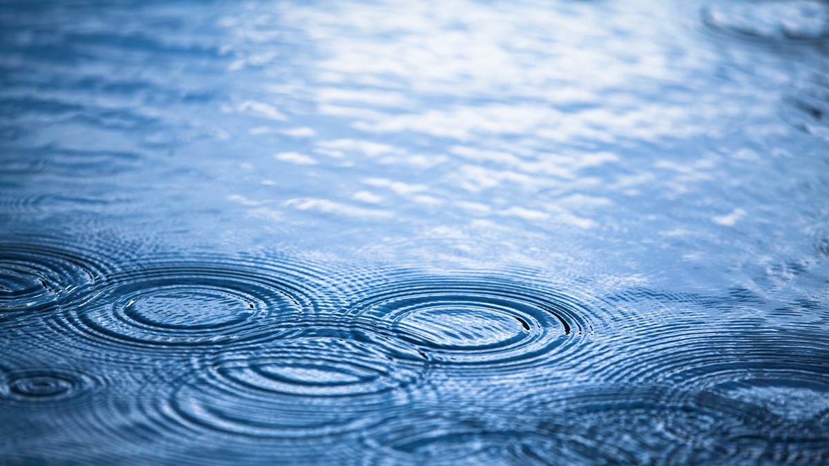 Surface of flood water with rain droplets landing on it.