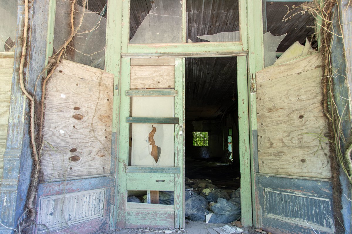 LykinsPhotos's tweet photo. Hushpuckena ~ A decade ago, a whim led me off U.S. Route 61 in Bolivar County onto a side road, where I stumbled upon Hushpuckena, a forgotten Delta hamlet named for abundant sunflowers in Choctaw. Its abandoned businesses, overtaken by vines and cracked pavement, whispered of a vibrant past. A rusted safe sat in the weeds, and the old R.C. Tibbs & Sons store still had its weathered doors. Today, the safe and doors are gone, the roof collapsed, and the brickwork crumbles, with sagging shelves in a nearby building surrendering to time. Abandoned North Mississippi~Echoes of the Past. @USAThroughTime