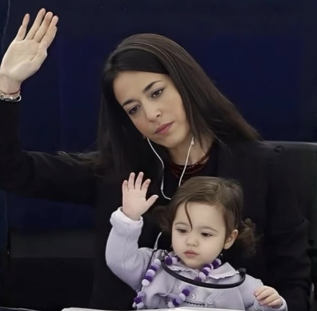 historyinmemes's tweet photo. An Italian politician brought her 44-day-old daughter to work and continued bringing her to work for the next three years.

Italian politician Licia Ronzulli famously brought her 44-day-old daughter, Vittoria, to the European Parliament in September 2010. As a breastfeeding mother without dedicated childcare facilities at work, she carried her baby in a sling while participating in parliamentary voting sessions.

Vittoria continued accompanying her mother to the chamber for the next three years, becoming a familiar sight in Parliament. As she grew older, she even began playfully raising her hand alongside her mother, mimicking Ronzulli during votes.