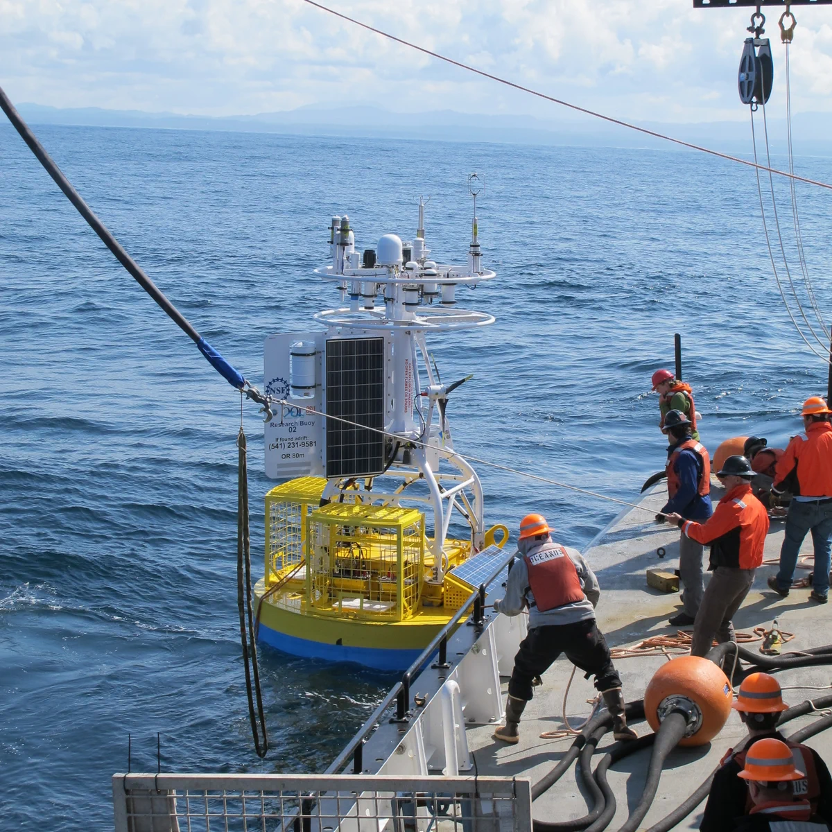 Workers on a ship releasing a scientific buoy into the ocean.