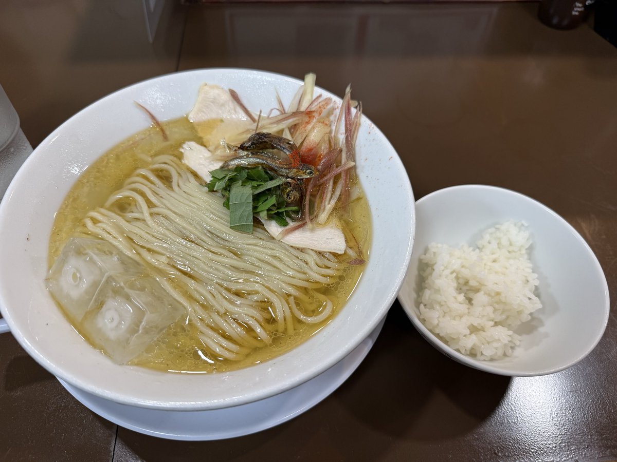 tabemeguri1's tweet photo. 那覇市前島
煮干し中華そば 加藤屋本店
限定麺B　1150円
大葉とミョウガの冷やし煮干しそば　小ライス付き

京都の人気店が沖縄に移転してきたとあって気になっていた店で、東京の蒲田にも修行された方の暖簾分けがあるほどの実力店

そんな背景もあって前々から足を運んでみたかったのだが、今回ついに訪問

初見なので定番の煮干しそばを食べようと思ってたが、妻が煮干しそばを選んだので今回私は敢えて限定麺を注文

それにしても自販機のメニューが意外に多くてどれを選べば良いのか結構悩んだ（煮干し、煮干しブラック、つけ麺、中華そば、油そば、白湯、限定麺など）

カウンター越しから渡された丼の中は透き通る黄金色の冷製スープにきれいに折りたたまれた細ストレート麺、ドカンと浮かぶ大きな氷

脇を固めるのはカリカリの煮干し、たっぷりのミョウガに大葉、そしてしっとりした鶏チャーシュー

視覚から涼を誘う見事な一杯

スープを啜ると、煮干しのクリアなダシの旨味が前面に出てきつつも、エグみは一切ない

冷水でシコシコに締められた麺は喉越しが良く、ミョウガのシャキッとした食感と大葉の薬味感が全体の味をキリッと引き締めてくれる

重たさがなく、暑い日でもスルスルと腹に入っていく食べやすさが秀逸

麺をあらかた平らげた後は、セットの一口ご飯に冷たいスープを注ぎ、残しておいた具材を乗せて〆のだし茶漬けへ

旨味の詰まった冷やしスープを吸った米と薬味の相性は抜群で、最後まで綺麗に食わせるストーリーが出来上がっている

夏の限定麺として実に完成度の高い一杯だった

4枚目に煮干しラーメンの写真を置いておく