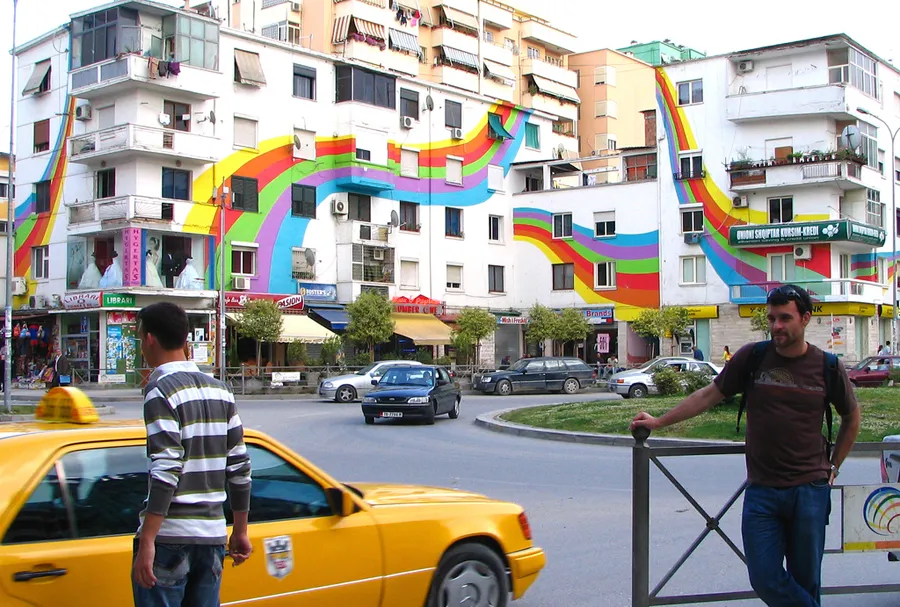 Yosoycorra's tweet photo. ¿Para qué sirve el arte?

Muchas personas se han hecho esta pregunta en la historia.

Pero, quizás, mi respuesta favorita la tienen estos edificios en Tirana, la capital de Albania.

En los años 90, Tirana era una ciudad gris. Literal y metafóricamente.

Después de 40 años de dictadura comunista, el ambiente de la ciudad era triste. La confianza en la política no existía y eso se reflejaba en el urbanismo.

La ciudad era un caos, con todos los servicios públicos destruidos.

A la ciudad llegó un nuevo alcalde con ganas de cambiar todo, de devolver la ciudad a sus ciudadanos.

Pero se encontró con un problema.

No había dinero.

No había presupuesto para obras públicas.

No había presupuesto para transporte.

No había presupuesto ni para farolas...

Entonces, ¿qué podemos hacer?, preguntó este alcalde.

Nada —respondieron sus asesores—, solo tenemos dinero para pintura.

Y aquello encendió una idea en su cabeza.

Porque aquel alcalde no era normal.

Aquel alcalde era Edi Rama, artista plástico antes que político.

Pintor y escultor, le habían traído a la política como ministro de Cultura y, después, había conseguido la alcaldía de la capital.

Así que... ¿tenemos dinero para pintura?—pensó el alcalde—pues pintaremos.

Lo primero que hizo fue seleccionar un edificio y planear su repintando... pero no de una forma cualquiera.

Eligió un color muy llamativo, eligió algo muy alejado del gris con el que el Partido Comunista había llenado las calles de Tirana.

Eligió pintarlo de naranja chillón.

Mientras los empleados del ayuntamiento pintaban la fachada, los vecinos salían a mirar y comentaban ¿Estos es una broma.

Es más, un funcionario de la Unión Europea intentó detener esta acción por ir contra la política urbanística europea.

Ante la resistencia inicial, el ayuntamiento decidió hacer una encuesta entre los vecinos...

Y los resultados fueron sorprendentes:

El 55% de los encuestados consideraban que el color elegido era feo o poco agradable.

Pero aquí viene lo interesante...

Para el 85% de la gente, el ayuntamiento debía seguir con el proyecto. Había que pintar las fachadas.

Porque lo importante no era el color, ni el gusto.

Lo importante era que, por fin, algo era diferente. El gris había desaparecido de la calle y había que seguir.

Así que el ayuntamiento se lo tomó en serio y decidió pintar todo el gris.

La capital se llenó de color.

Así, Tirana se convirtió en la ciudad de las fachadas de colores.

Pero lo que nadie esperaba fueron las consecuencias.

Los vecinos de esas casas, las que se pintaban, no las que aún continuaban grises, comenzaron a hacer algo que hasta entonces no hacían... Pagar impuestos.

El habitual 5% de población que pagaba en aquellos impuestos pasaba a rangos del 90% en esos edificios.

Y esto se debía solo a una razón: confiaban en que su dinero servía para algo.

Para convertir la ciudad en una obra de arte.

Pero lo más inesperado de todo fue lo siguiente: En las manzanas con edificios llenos de colores, bajó el número de delitos.

La razón era simple y la dijo el propio alcalde: nadie está dispuesto a robar delante de una obra de arte.

Así que, contestando a la pregunta del principio: ¿Para qué sirve el arte?

Pues para vivir mejor.

Nadie sabe cómo, ni por qué... pero estar rodeado de arte nos hace mejor sociedad, más civilizados, nos hace... ser más humanos.

Y en estos tiempos que todo parece más gris y más oscuro, creo que vivimos la peor crisis de todas: la de la falta de optimismo.

Ahora que nadie piensa que el futuro vaya a ser mejor, de vez en cuando me encuentro con un edificio pintado de colores o con una publicación en redes sociales que me hace la vida mejor.

Y entonces, por un momento pienso en que quizás sí, que esa mínima parte de mí ha resonado y puede que algún día, nuestras calles se vuelvan a pintar de color y cada fachada sea una fiesta.

Si una vez Tirana lo consiguió, ¿por qué no nosotros?

Gracias por leer hasta el final esta historia y, si te ha gustado, me haces un favor si retuiteas, comentas o le das un like.