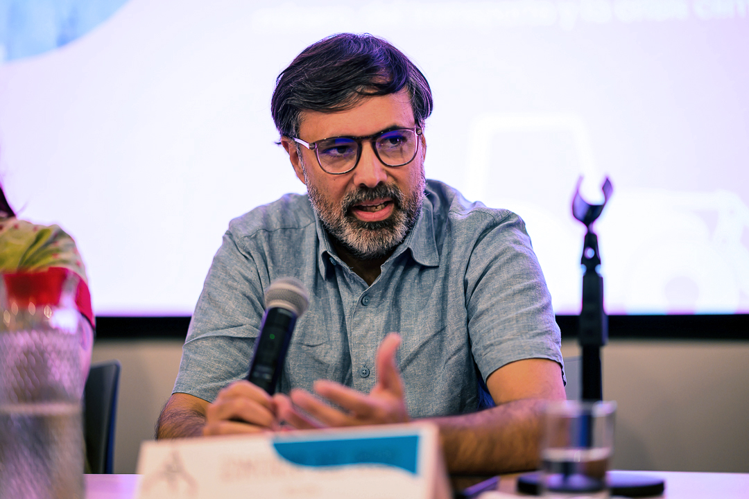 Primer plano de Edmundo Del Pozo, de la DGDHJP de la SCJN, en un panel de diálogo, sentado ante una mesa con micrófono, interviniendo durante la presentación de un informe sobre conflictos socioambientales, extractivismo, territorio y derechos humanos. Al fondo se observa una pantalla proyectada.