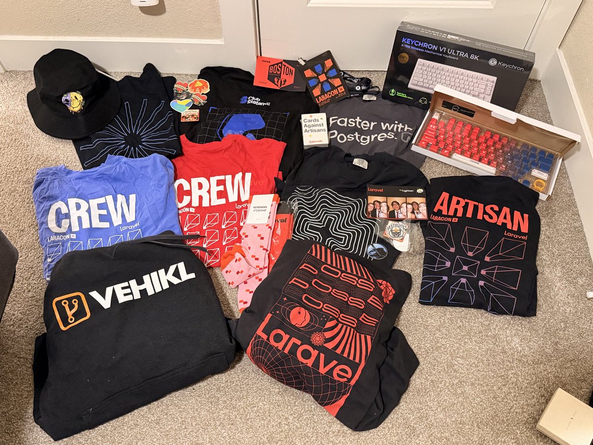 A layout of so many tech t-shirts, hoodies, stickers, socks, a mechanical keyboard, and custom keycaps that Leah collected from Laracon US.