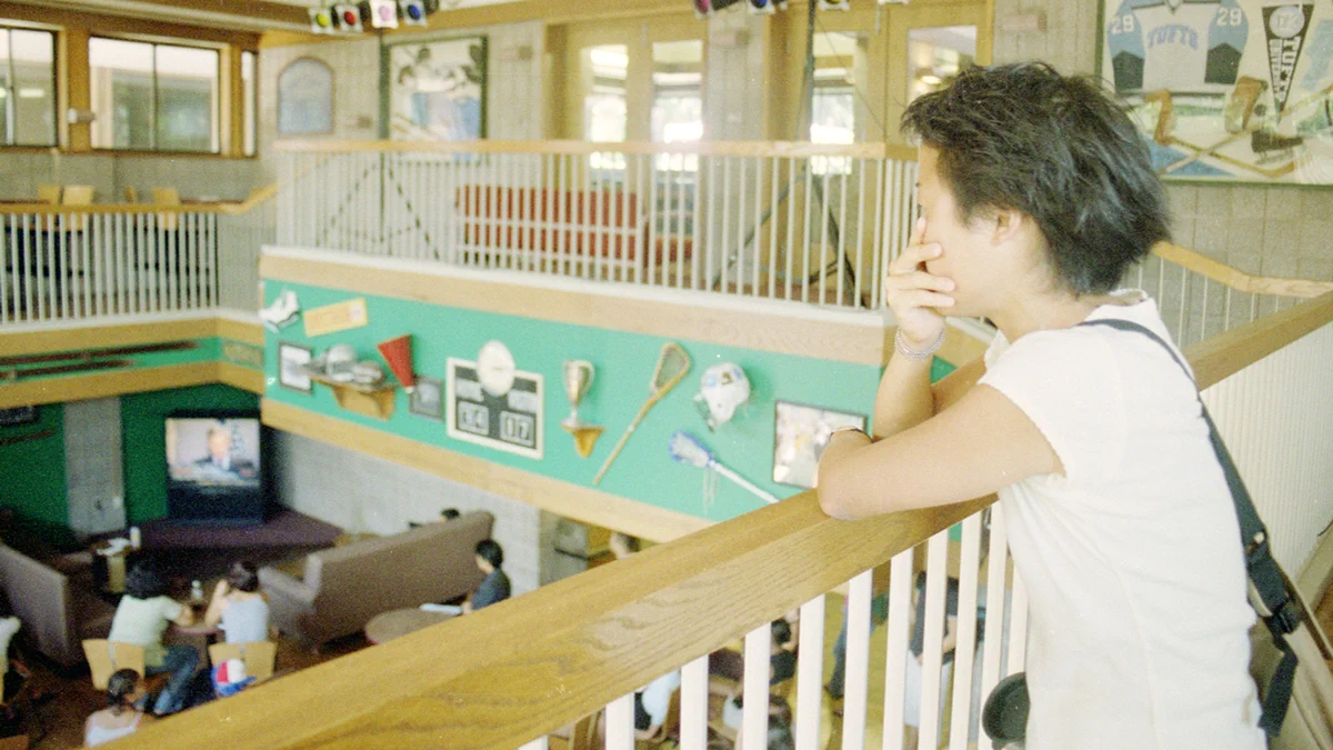 On September 11, 2001, a student watches the television in the campus center from the second floor railing as they cover their mouth in shock as events unfold across the country. Photo: Tufts Archival Research Center