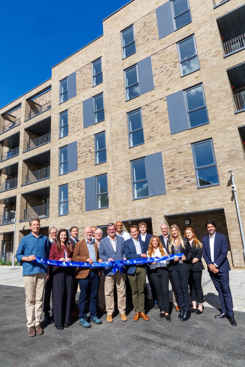 A group of people smile outside of the new Len Martin Court development. They hold a large blue ribbon between them