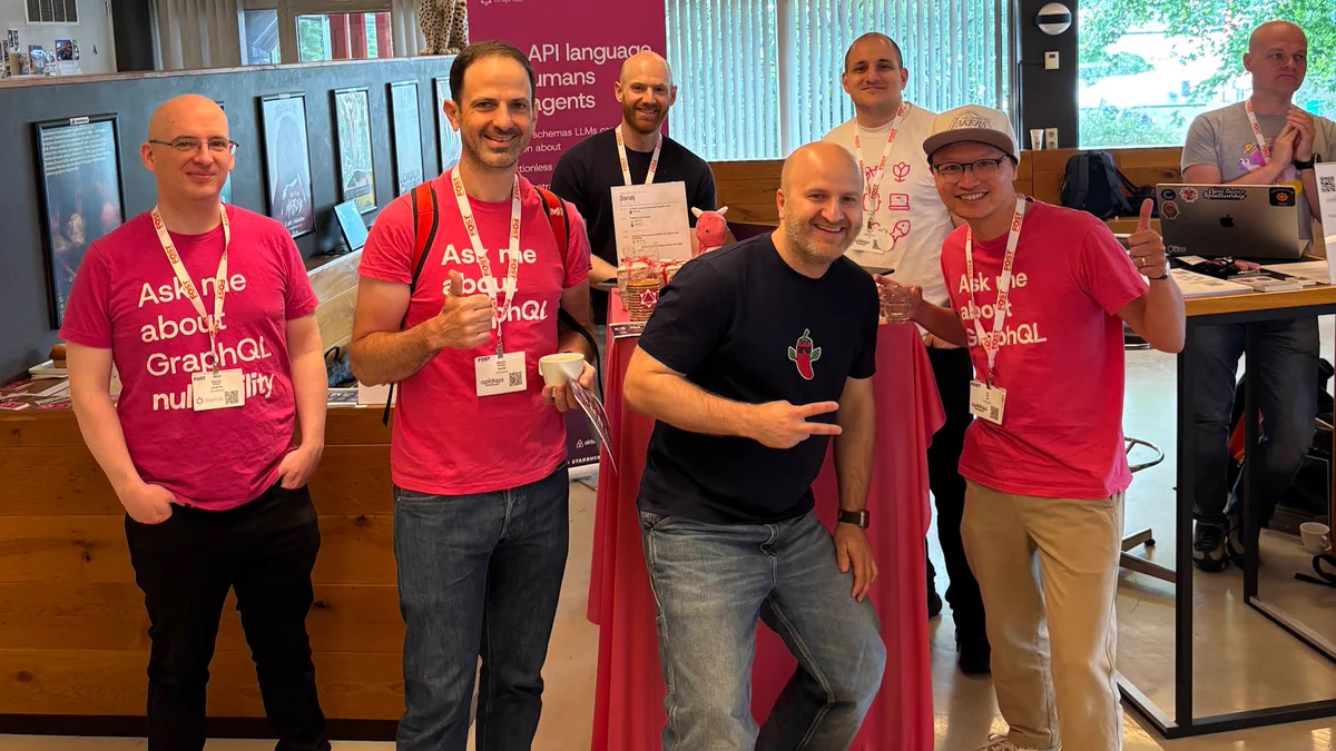 A group of people in pink shirts celebrating at an event, smiling and engaging at a booth with promotional materials.