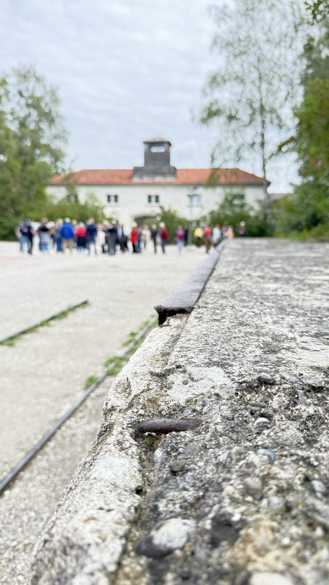 BattlefieldDisc's tweet photo. Ruins of a former unloading dock with railway tracks next to them are still visible in front of the old guardhouse and entrance of former Dachau concentration camp. Though the unloading docks were used for goods and not for people, the image is a poignant reminder of what happened in several other camps built to the standards invented and perfected at Dachau. 
Visited today on the @WWIImuseum #easycompany tour.