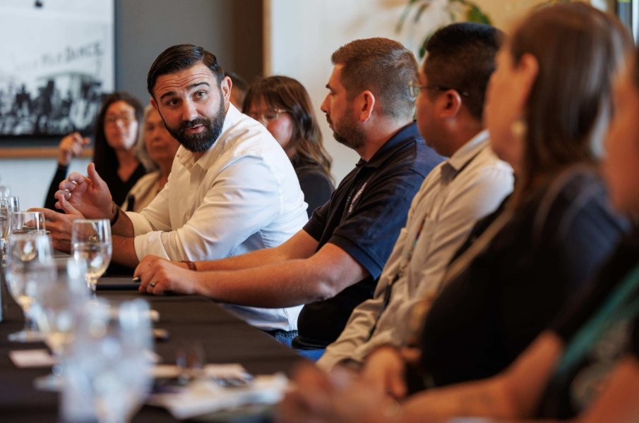 Administrator Cameron Hamilton in a white shirt actively speaking during a group meeting at a long table with attentive colleagues.
