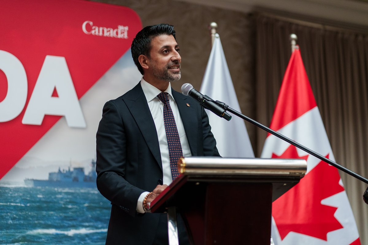 Minister Sidhu delivering remarks with the Canada flag in the background