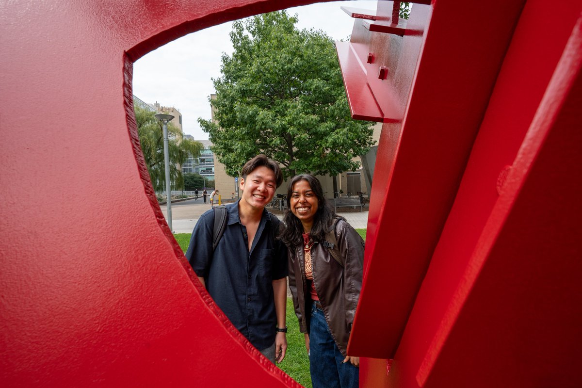 Two people standing near a red public sculpture on MIT's campus