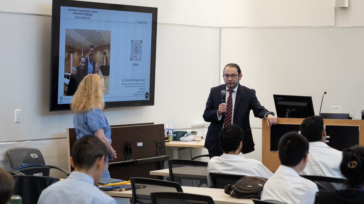 Guest speaker Carlos Rodriguez Aceves, MD, stands beside a lectern holding a microphone as he answers questions from the audience.
