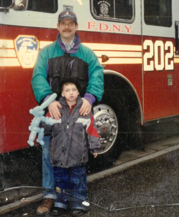 A person and a child are standing in front of an FDNY fire truck, numbered 202. 