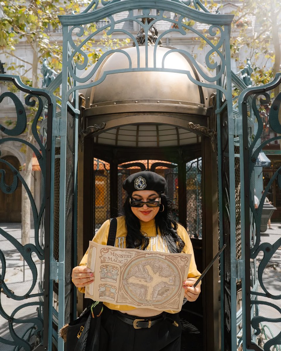 Girl dressed in a Hufflepuff outfit posing with a wand map, featuring an atmospheric shot of Place Cach\u00E9e in The Wizarding World of Harry Potter - Ministry of Magic at Epic Universe.