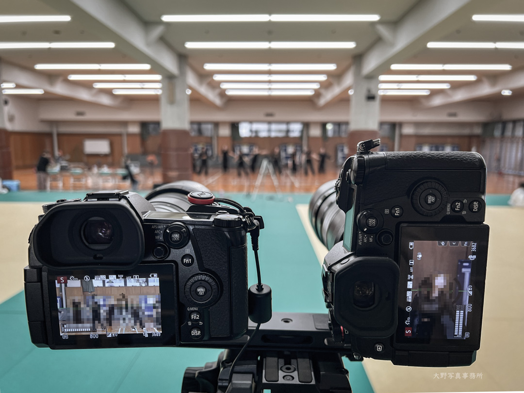 oonoakila's tweet photo. とあるイベント撮影の仕事の撮影条件確認のためリハーサルにお邪魔させていただきました。被写体まで約25m程度の距離で300mm（換算600mm）は寄りすぎ、かつ縦グリップを着けた方が良さそう。1.4倍テレコンを着けた40-150mm の望遠端で換算420mmで指先から足先まで入る。左手に付け替えたパン棒を握りながら左手でレリーズシャッターを切り、右手で縦撮影にすることで同時にも撮れそう。体育館と思ったら武道場だったけど保護用のマットを持参して正解。このシステムで他のイベントにも応用できそう。足元には手持ちサブとしてSONY機。