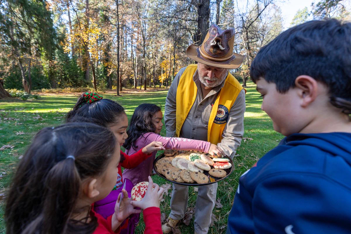 State parks volunteer distributing cookies to children outside at Empire Mine State Historic Park.