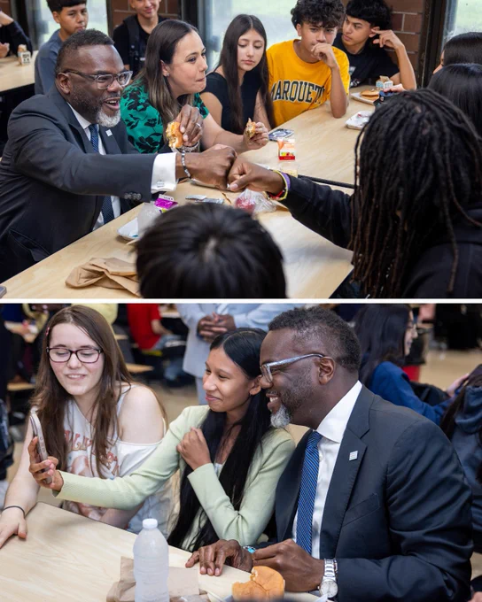 
3. TOP: Mayor Johnson sitting at lunch table with students, fist bumping a boy at Curie High School with one hand, holding a half-eaten sandwich in the other. BOTTOM: Mayor Johnson taking selfie with two female students at Curie High School lunch table. 