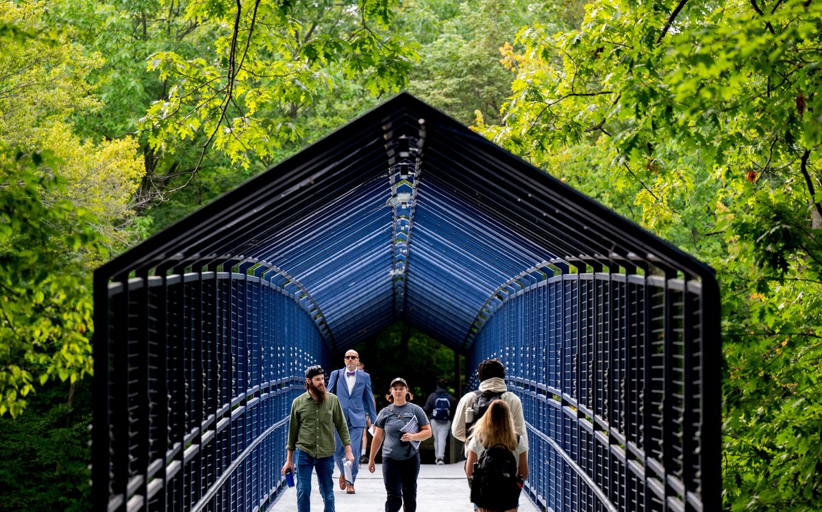 Four people, including a man wearing a blue suit and bow tie, cross the Little Mac Bridge.