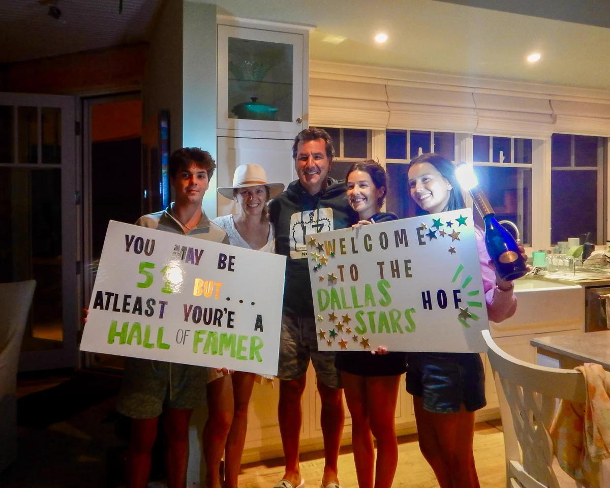 Marty Turco poses at home with his family members holding signs that read “you may be 51 but at least you’re a hall of famer” and “welcome to the Dallas Stars HOF”