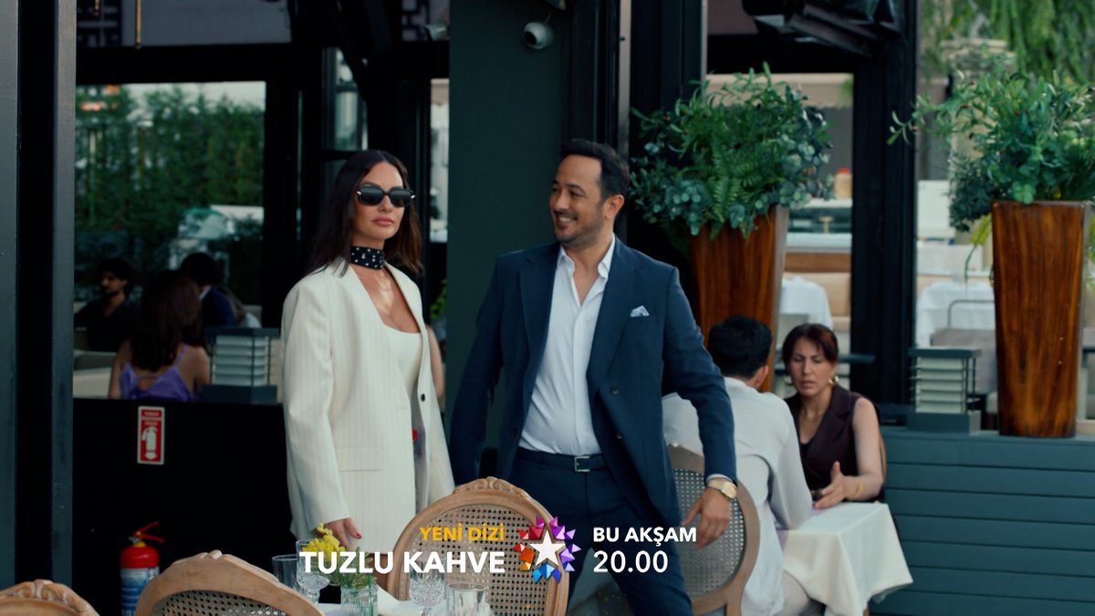 A stylish woman in a white blazer and sunglasses walks arm-in-arm with a smiling man in a navy suit through an upscale restaurant terrace, with on-screen text promoting the new series "Tuzlu Kahve" airing at 20:00 on Star TV—visually teasing the elegant, character-driven drama fans are eagerly anticipating.