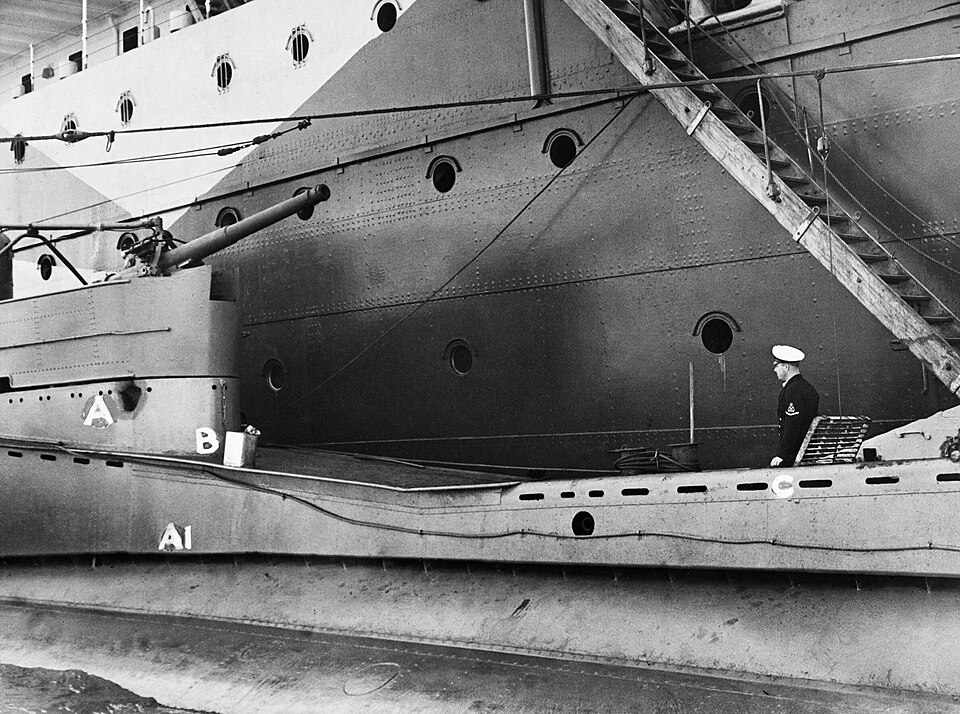 HeroesOfBritain's tweet photo. Petty Officer Tommy Gould lay flat on his back inside the casing of HMS Thrasher with an unexploded bomb in his arms. Lieutenant Peter Roberts was in front of him, pulling him through the darkness by the shoulders. Every time the bomb moved, it made a loud twanging noise, like a broken spring.

Hours earlier, on 16 February 1942, Thrasher had sunk a heavily escorted supply ship off Crete. Enemy escorts and aircraft answered with depth charges and bombs. The submarine dived and survived. After dark she surfaced to recharge her batteries. As the boat rolled in the swell, the crew heard something heavy banging above the pressure hull.

It was an unexploded bomb. Gould and Roberts volunteered to deal with it. They steadied it, wrapped it in a sack, secured it with rope and manhandled it forward until it could be dropped over the bows while Thrasher backed away.

Then they found a jagged hole in the casing, and beneath it a second bomb was lying on top of the pressure hull. It could not simply be lifted back through the hole. The only workable route was through a cramped space beneath the casing to a metal hatch about 20 feet away. In places there was barely room to lie full length.

Gould and Roberts lowered themselves in and wriggled towards the bomb with only a shaded light. Gould got onto his back and held the weapon against him while Roberts dragged him towards the hatch. They knew what would happen if an enemy aircraft or ship appeared: Thrasher would have to crash-dive. 

The two men outside the pressure hull would be drowned.
For roughly 40 minutes they pushed, pulled and eased the bomb through the darkness until they could get it out, carry it forward and lower it over the side.

 I recovered a photograph of the damaged casing; it marks where the bombs struck and shows Gould standing at the hatch through which the second one was dragged.

Roberts and Gould were both awarded the Victoria Cross. The official citation noted that Thrasher was still close to the enemy coast and that the men knew a forced dive could kill them. Gould later remembered coming back inside soaked through. The captain’s response was only: “You’d better get yourselves dried.”