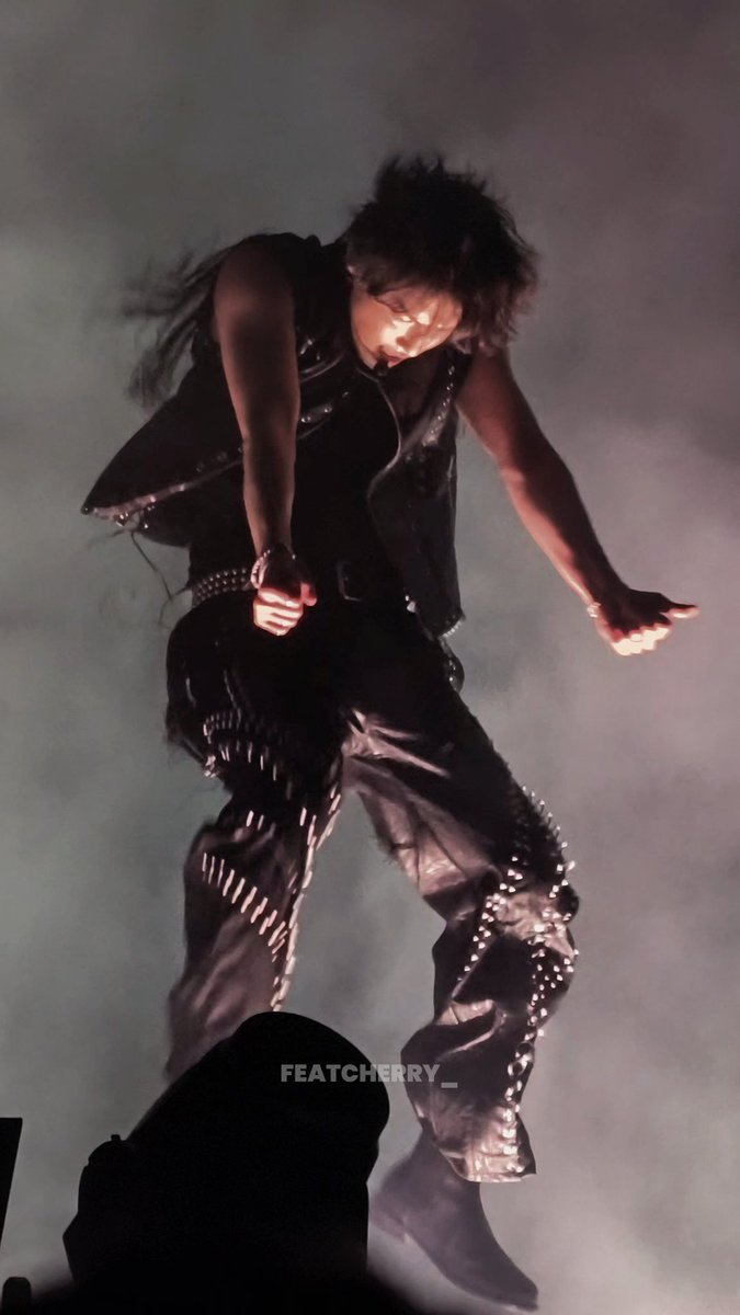 A performer wearing a studded black leather vest and pants jumps or dances on stage amid smoke, with the watermark 'FEATCHERRY_' displayed across the image.