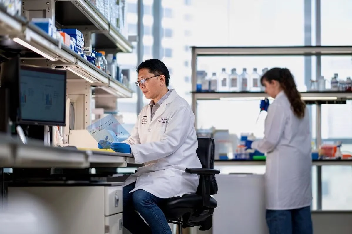 Dr. Boyi Gan works at a lab bench while a research assistant uses a pipette in the background at The University of Texas MD Anderson Cancer Center.