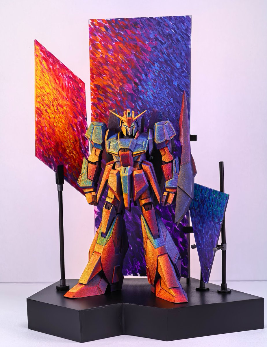 _FL4V4_'s tweet photo. 点彩ZETA、展示まで含めて完成しました。

最後に作ったのが、機体を囲む背景パネルです。
ZETA本体に描いた夕陽、赤紫の雲、青い空の色を、そのまま周囲の空間にも広げてみました。
パネルは一枚につなげず、暖色、暖色から寒色への移り変わり、寒色をそれぞれ別の面として配置しています。
少し角度を変えるだけで重なり方や見える色の割合が変わるので、機体と一緒に立体的な色の構成として見られるようになりました。

背景にも本体と近い筆致を使っています。
離れて見ると光や空気のかたまりに見えて、近づくと一つ一つの筆跡が残っている、この感じは今回かなり気に入っています。
ZETA本体を塗り始めた時に考えていた「夕方の光」を、最後に展示全体まで広げることができました。
これでひとまず完成です。

#Zガンダム #ZETA #ガンプラ #筆塗り #点彩 #模型制作