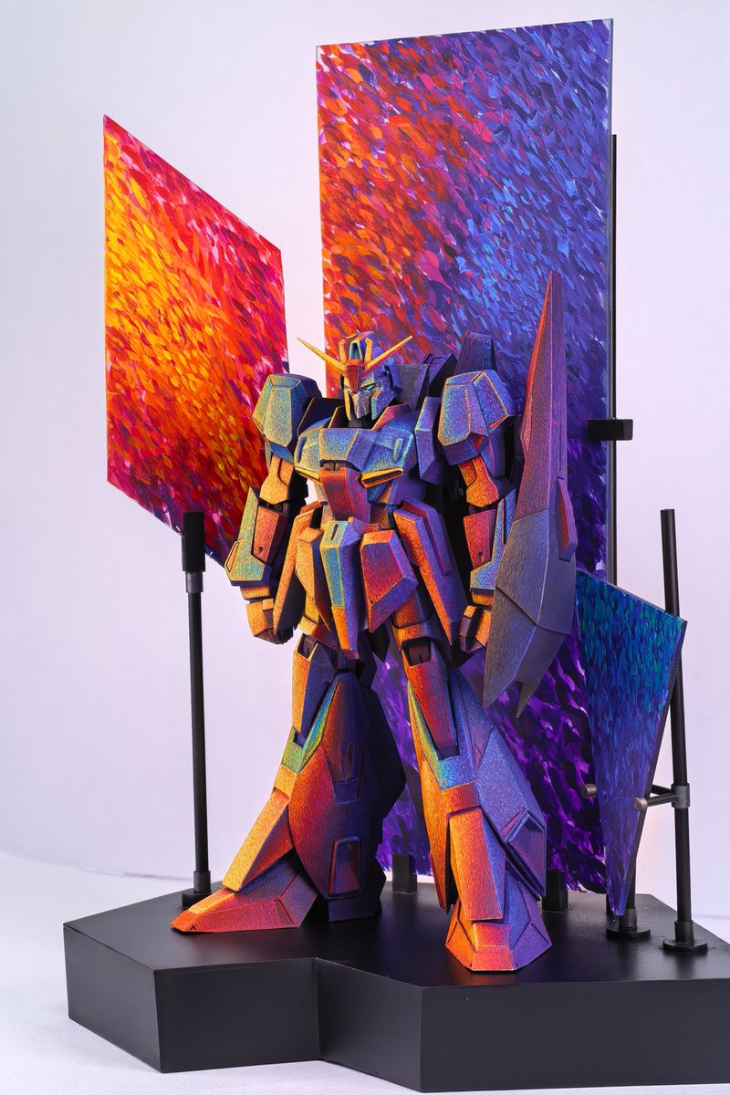 _FL4V4_'s tweet photo. 点彩ZETA、展示まで含めて完成しました。

最後に作ったのが、機体を囲む背景パネルです。
ZETA本体に描いた夕陽、赤紫の雲、青い空の色を、そのまま周囲の空間にも広げてみました。
パネルは一枚につなげず、暖色、暖色から寒色への移り変わり、寒色をそれぞれ別の面として配置しています。
少し角度を変えるだけで重なり方や見える色の割合が変わるので、機体と一緒に立体的な色の構成として見られるようになりました。

背景にも本体と近い筆致を使っています。
離れて見ると光や空気のかたまりに見えて、近づくと一つ一つの筆跡が残っている、この感じは今回かなり気に入っています。
ZETA本体を塗り始めた時に考えていた「夕方の光」を、最後に展示全体まで広げることができました。
これでひとまず完成です。

#Zガンダム #ZETA #ガンプラ #筆塗り #点彩 #模型制作