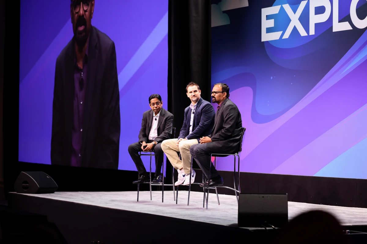 Three people on a large key note speaking stage at VMware Explore. 
