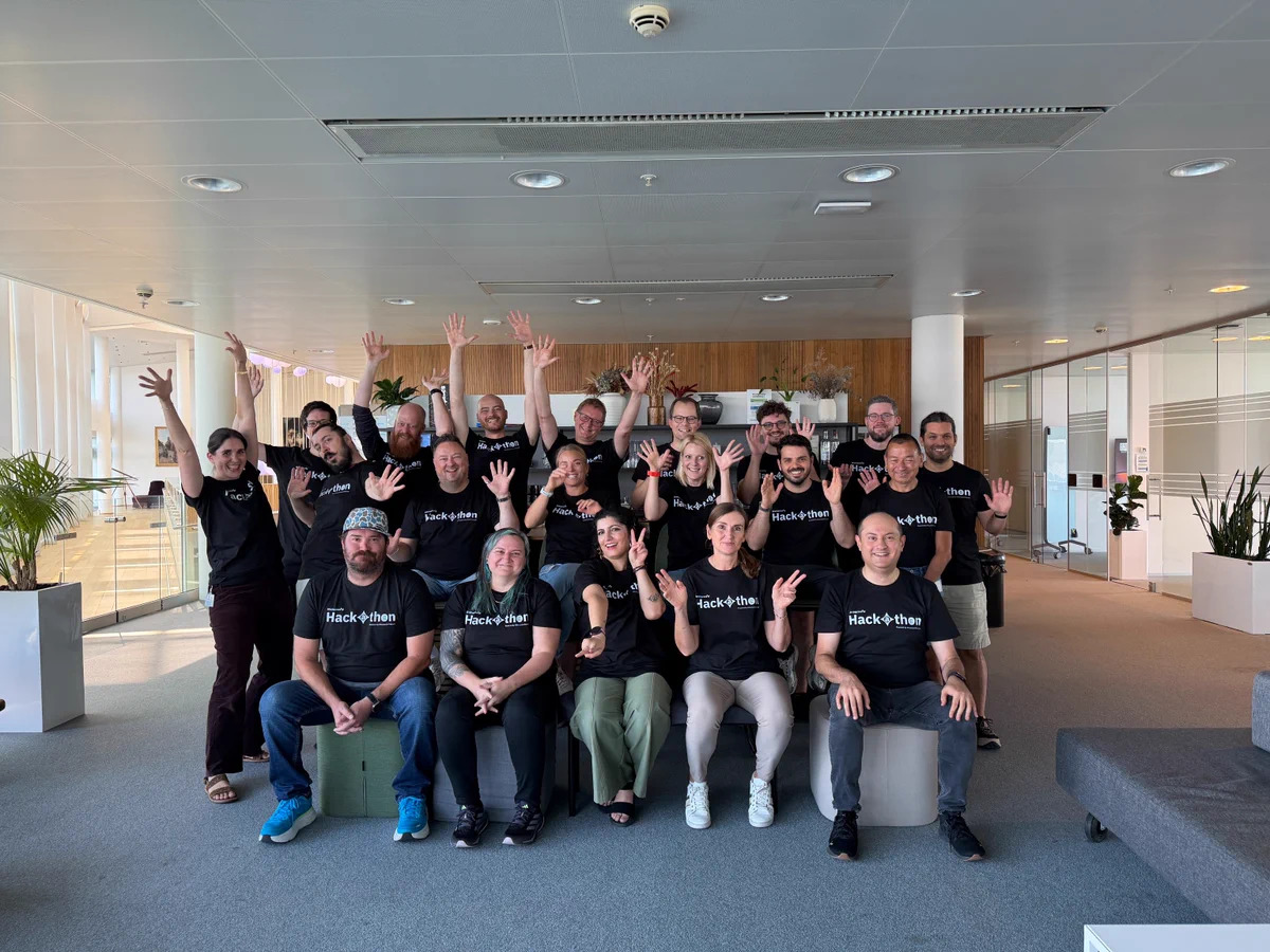 About twenty Copenhagen engineering and product Siteimprovers pose together in matching black Hackathon 2026 shirts, arms raised in celebration inside their office lobby.