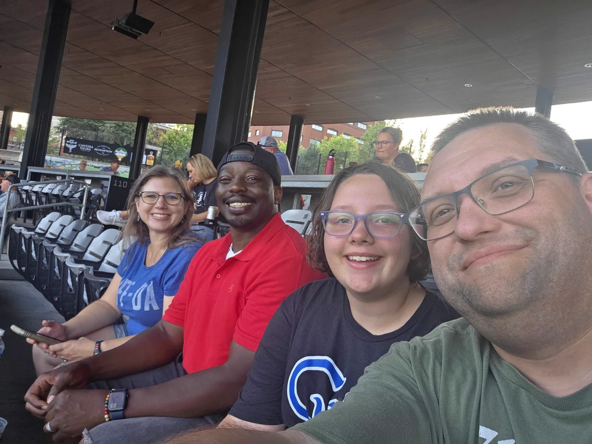 Four Minneapolis Siteimprovers smile for a selfie in the stands at a minor league baseball game.