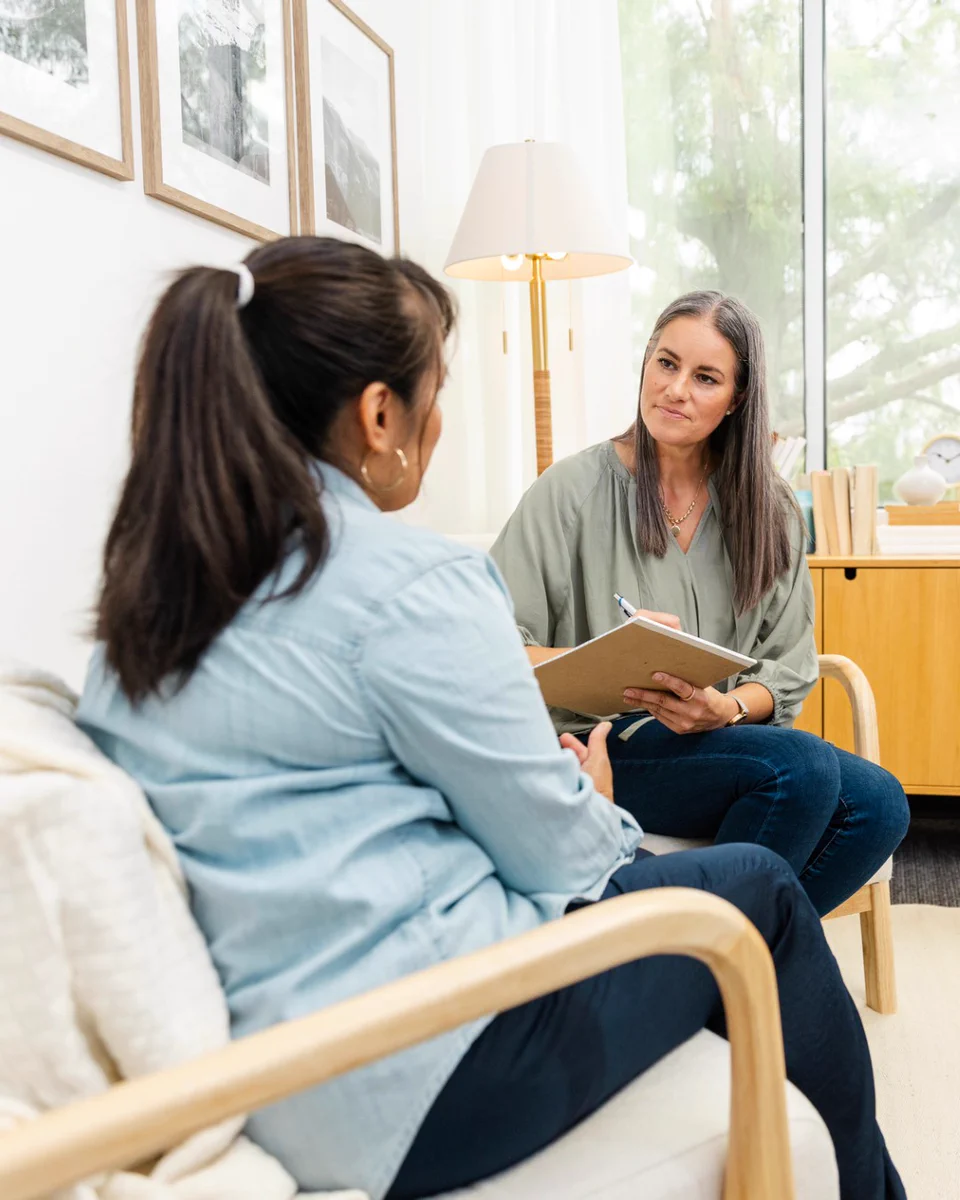 Sitting together in a therapist's office, a woman client shares as the adult counselor takes notes.