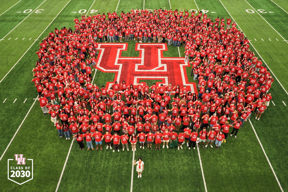 The Class of 2030 poses for a picture with President Renu Khator at the Indoor Practice Facility, surrounding a UH logo.