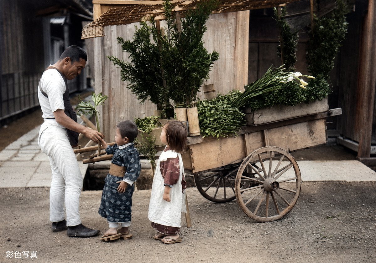 old_nippon's tweet photo. 大正時代初期（1914年頃）に撮影された、荷車を引く花売りと子どもたち。着物姿の小さな子どもと、行商人の男性がやり取りをしている日常の風景。当時の人々の服装や生活様式、当時の空気感が伝わってきます。※彩色写真 https://t.co/A7os80JL4p