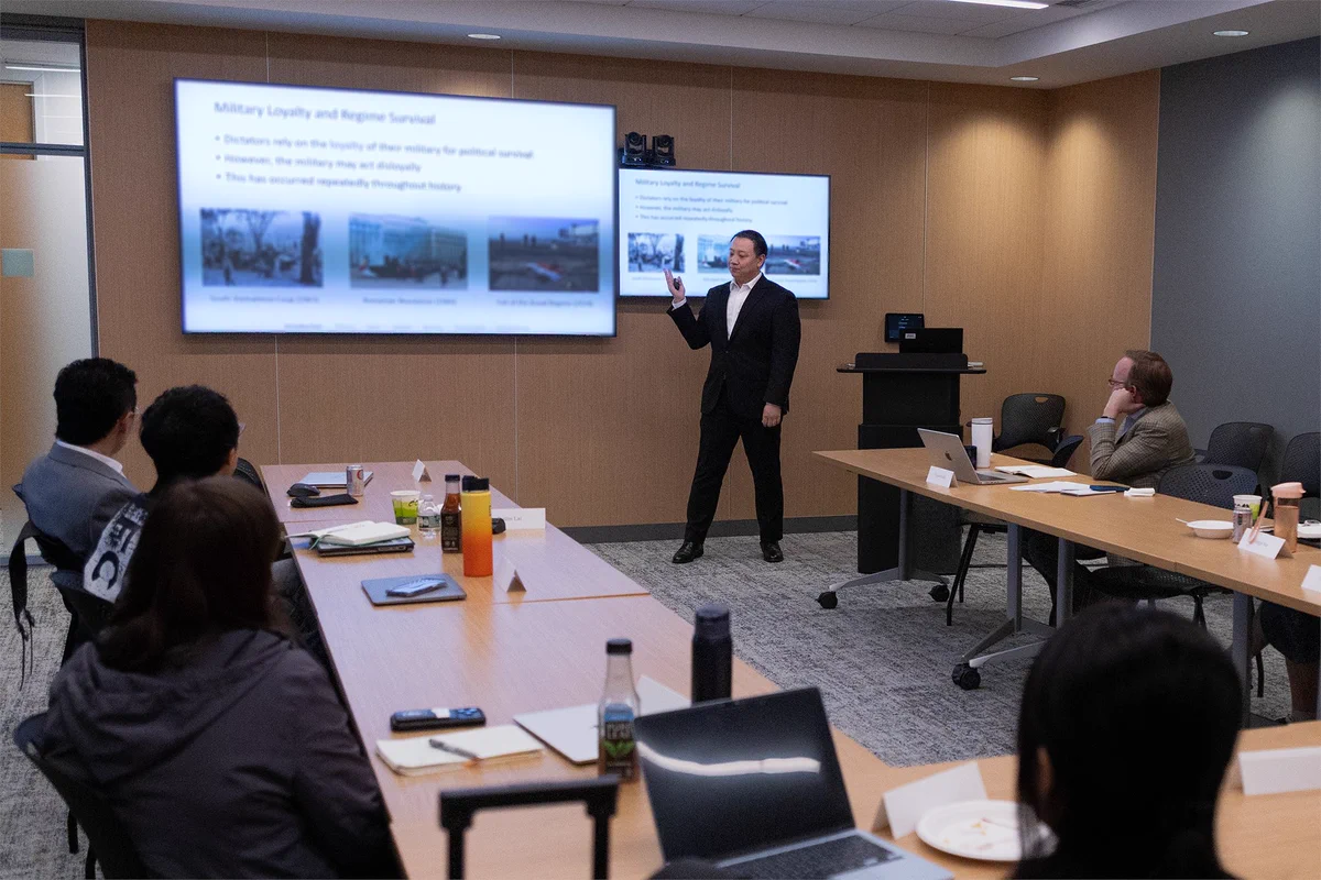A person is giving a presentation at the front of a room full of people.