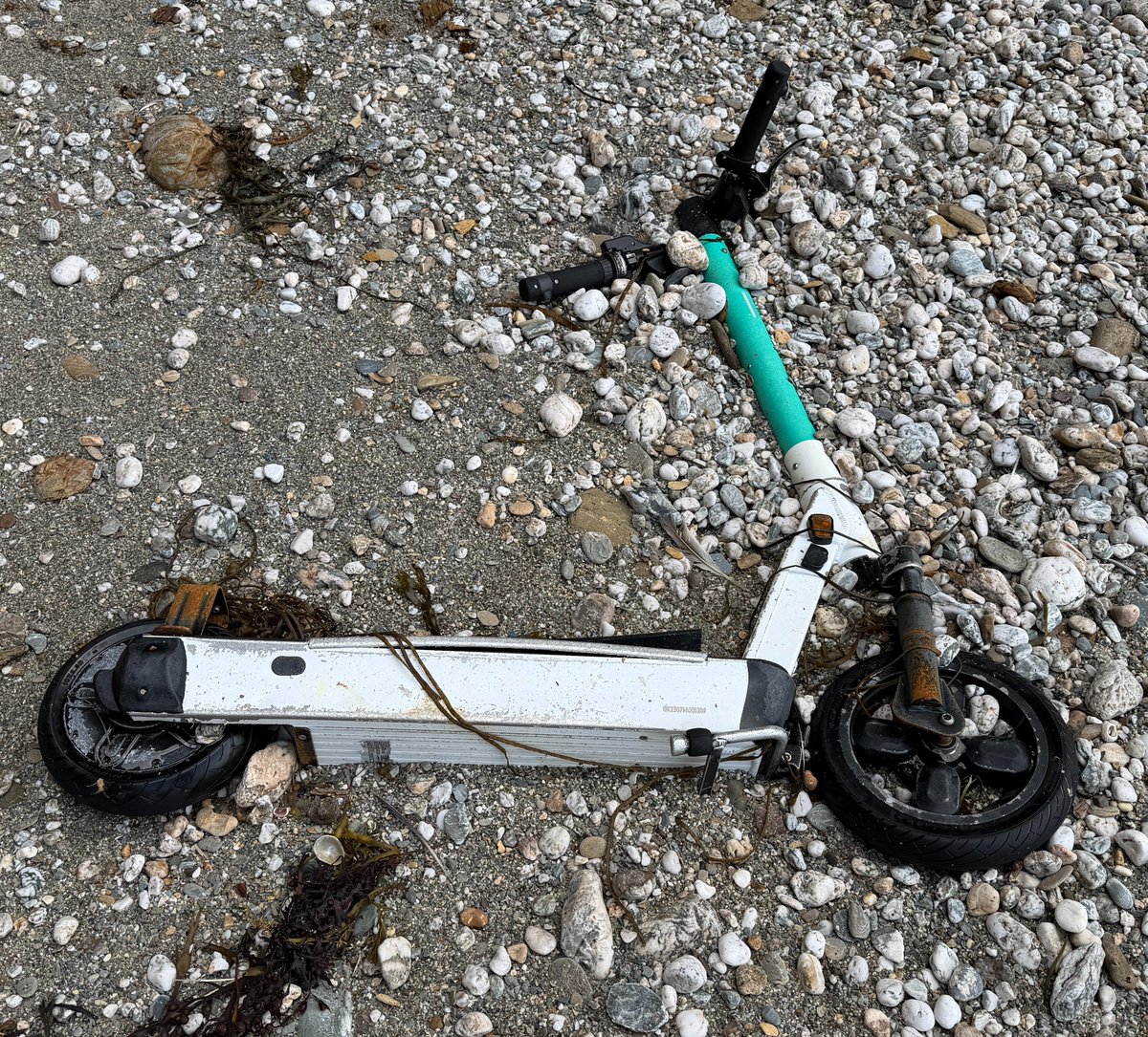 e-scooter lying among pebbles at base of cliff