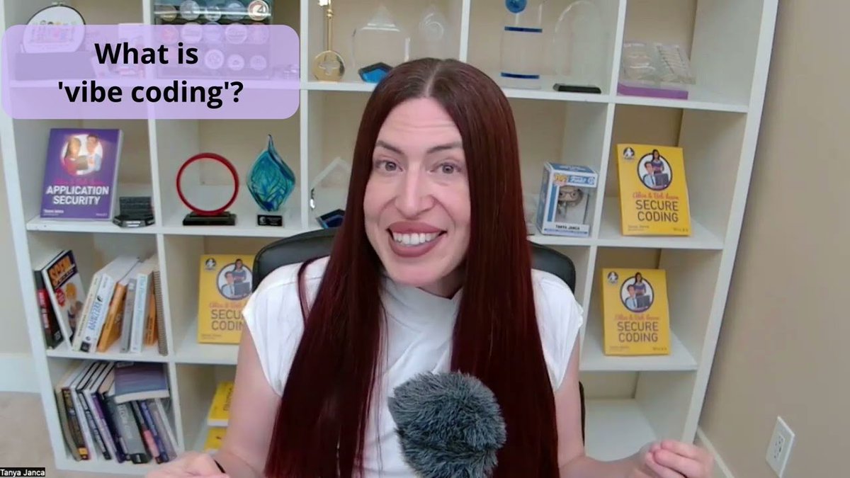 A woman with long dark red hair speaks in a home office, seated in front of white shelves with books and awards, including several titled Secure Coding and Application Security. A purple text box reads What is vibe coding? and a name label at the bottom left says Tanya Janca.
