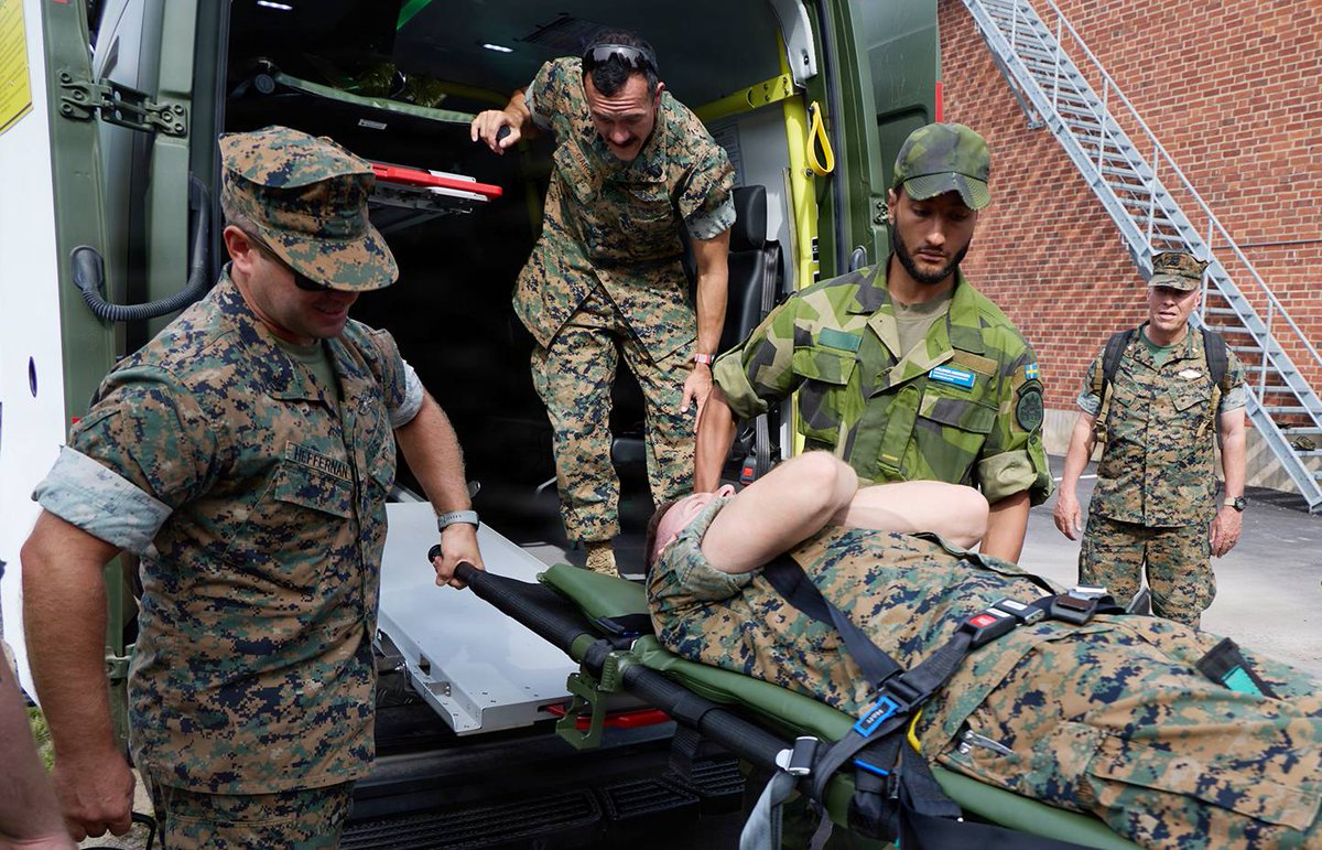 U.S. Navy corpsmen and a Swedish service member load a simulated casualty into a military ambulance during medical training.