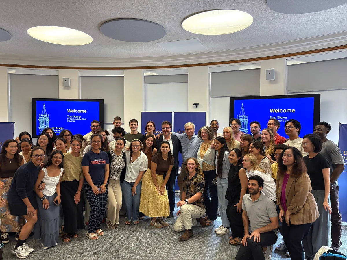A large group of students and staff gathered and smiling for a group photo with Tom Steyer in a lecture room.