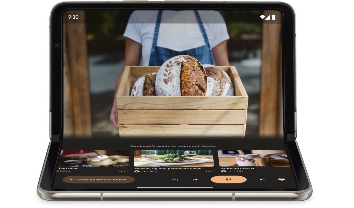 A foldable smartphone is partially unfolded in a tabletop position, showing a video player app