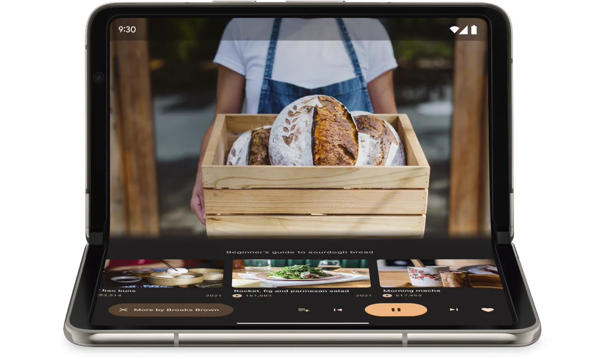 A foldable smartphone is partially unfolded in a tabletop position, showing a video player app