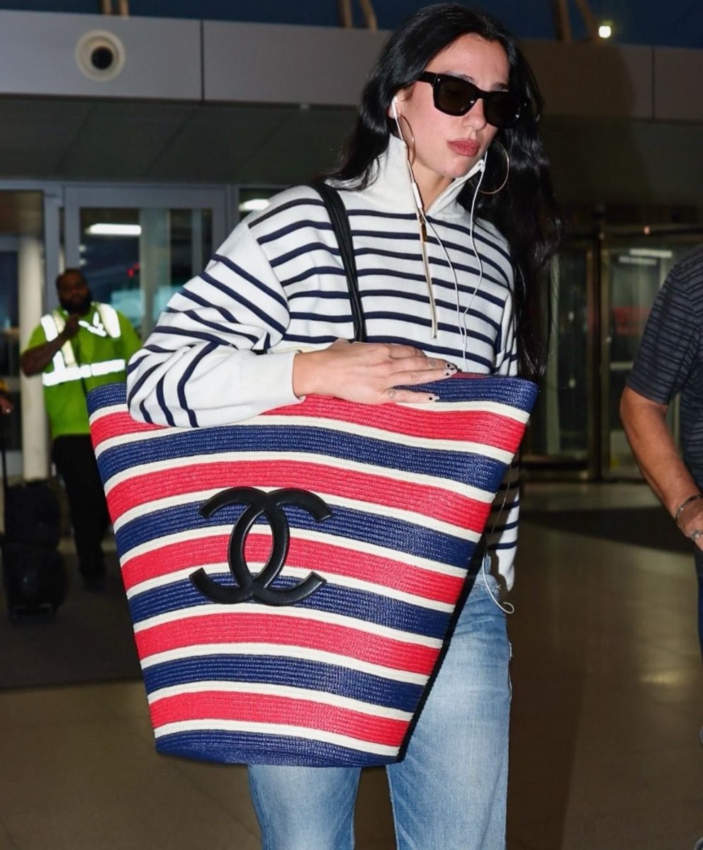 teodara's tweet photo. Dua Lipa arrived at JFK with a standout accessory from Matthieu Blazy’s latest Chanel Cruise collection: an extra-large woven tote, styled with nautical stripes for a vacation-ready look. https://t.co/PUzqJ0AZYI