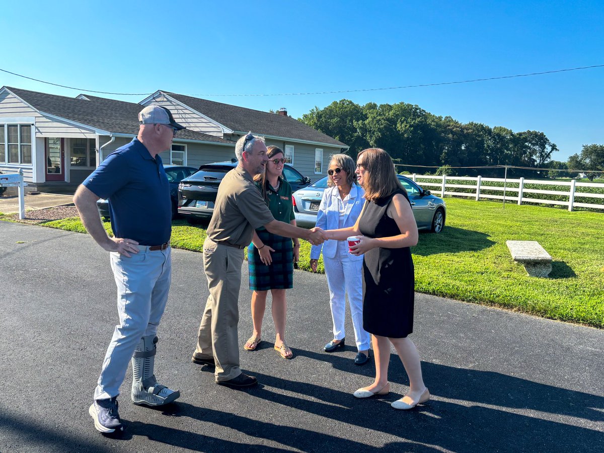 Rep. McBride, standing next to Sen. Lisa Blunt Rochester, and holding a coffee, shakes hands with an attendee at the Ard Na Gréine event.
