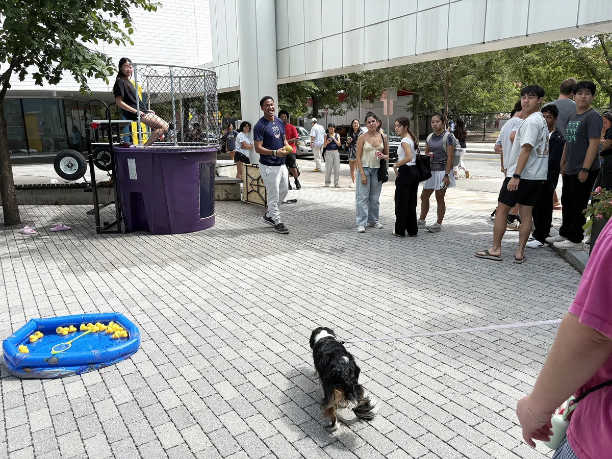 A group of students watch as a student sits in a dunk tank. A dog watches from a distance.