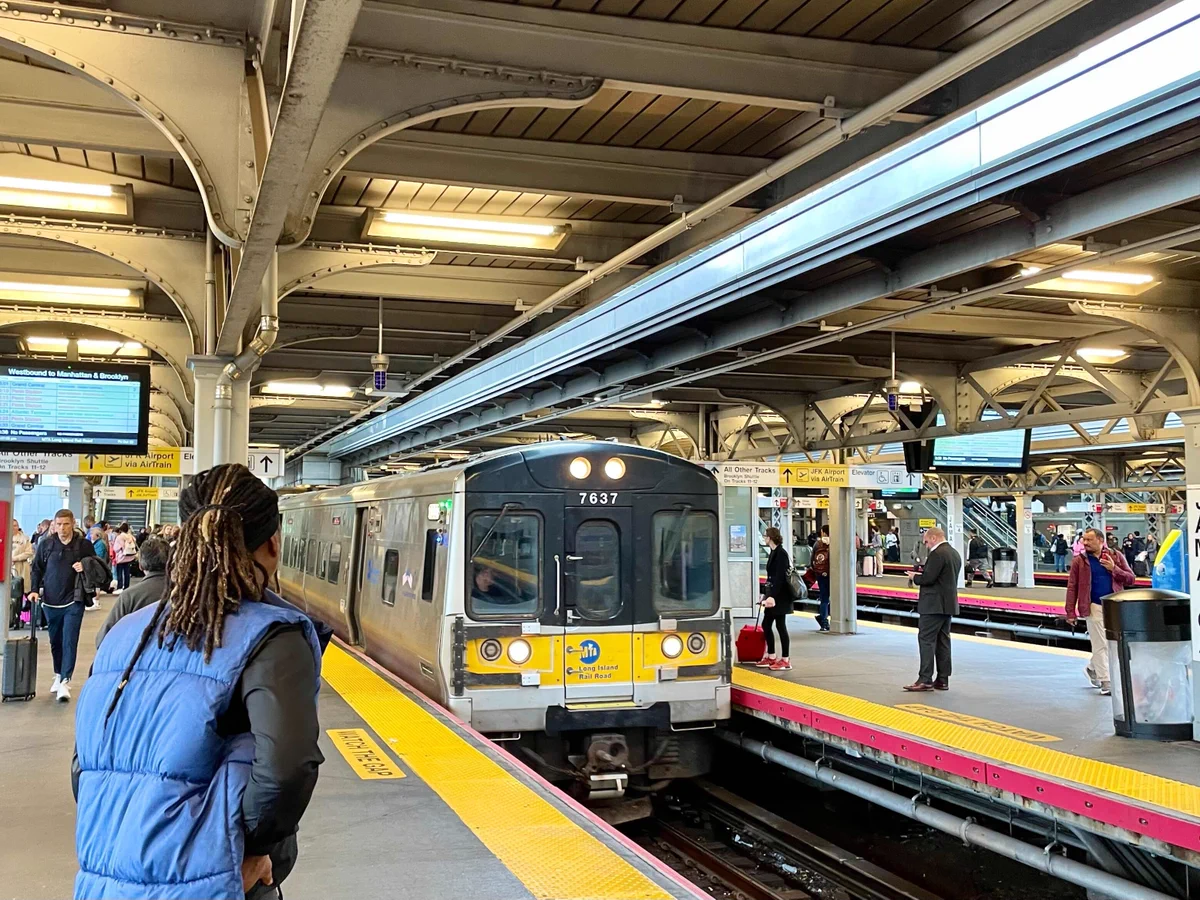 People standing and waiting at the Jamaica station platform as an LIRR train pulls into the station.