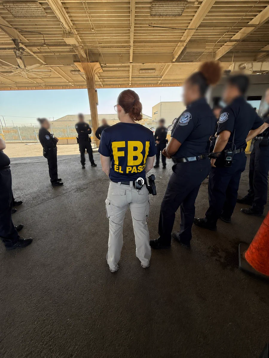 FBI agent from El Paso stands with law enforcement officers under a covered outdoor area during a briefing.